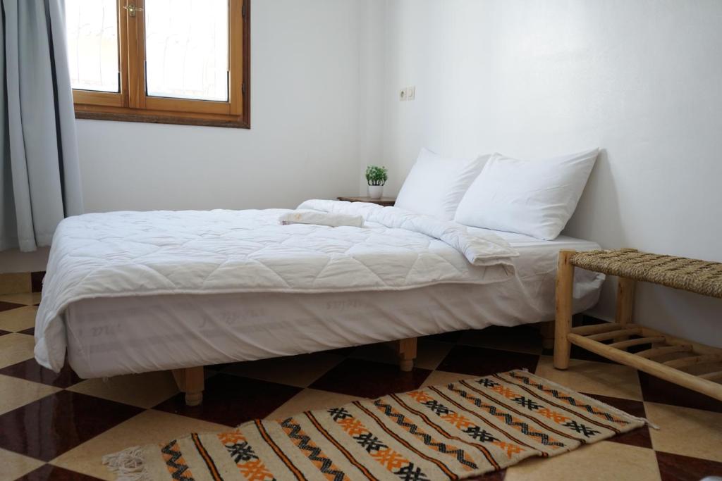 A simple bedroom featuring a bed with white bedding and a patterned rug on the floor.